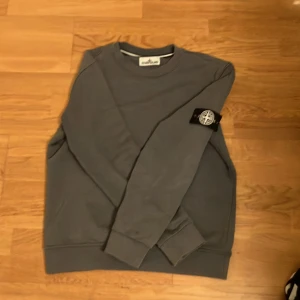 Grå sweatshirt från Stone Island - Säljer en stilren grå sweatshirt från Stone Island med deras ikoniska märke på ärmen. Tröjan har en klassisk passform och är perfekt för en avslappnad look. Tillverkad i mjukt material för extra komfort. Storlek M men passar S