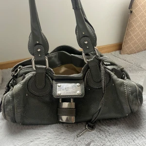 Chloe paddington väska - Lägger ut denna väska igen, söker snabbaffär och enbart seriösa köpare! Kan mötas upp i sthlm elr posta💕Färg: mörkgrön/grå se bilder! Fint skick, finns några skavanker såsom att färgen är lite skavd på sidorna men inget som syns när man använder den. Även lite ”smutsig” inuti men inte särkilt mkt. Nypris på väskan ligger på ca 15000 kr. Äkthetbevis finns . 4000 kr är fast pris då jag redan sänkt från 4500 kr! 