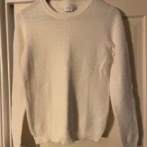 Vit stickad/virkad tröja från VILA - Säljer en stilren vit stickad tröja från VILA. Tröjan har en rund halsringning och långa ärmar, perfekt för kyligare dagar. Den har en fin textur och ribbstickade muddar vid ärmslut och nederkant.