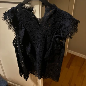 Mörkblå spets topp - Elegant mörkblå topp i spets från Zara med korta ärmar och v-ringad design. Perfekt för speciella tillfällen med sin fina spetsdetaljering.
