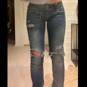 Blå slitna jeans - Snygga blå jeans med slitningar och hål på knäna. I fint skick. Jeansen sitter låg midja med en mindre utsvängnign men långt i fåren slim fit  eller straight leg.