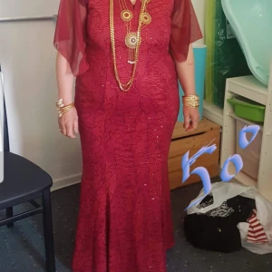 Vinröd klänning med spetsdetaljer - Elegant vinröd klänning med spetsdetaljer och korta ärmar i transparent material. Klänningen har en figurnära passform och är dekorerad med ett subtilt mönster. Perfekt för festliga tillfällen.