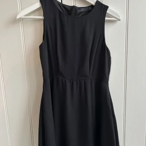 Svart ärmlös klänning från By Jeppson - Elegant svart ärmlös klänning från By Jeppson. Perfekt för en stilren look med sin enkla design och klassiska snitt. Klänningen har en rund hals och en smickrande passform. Använd en gång.