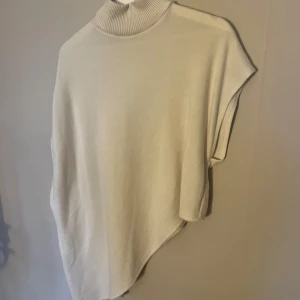 Vit poncho från Zara - Säljer en stilren vit poncho liknande från Zara med polokrage. Perfekt för lager-på-lager under kyliga dagar. Den har en asymmetrisk design som ger en modern touch. Passar bra till både jeans och kjol.