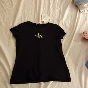 Svart t-shirt från Calvin Klein - Snygg svart t-shirt från Calvin Klein med deras ikoniska logga tryckt på bröstet. Perfekt för en stilren och avslappnad look. Kortärmad och tillverkad i mjukt material för extra komfort. Helt oanvänd pris kan diskuteras 