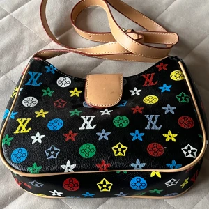 Färgglad axelväska med monogram - Snygg axelväska med färgglatt monogrammönster på svart bakgrund. Väskan har en justerbar axelrem i ljusbrunt skinn och en praktisk stängning med tryckknapp. Perfekt för att ge en färgklick till din outfit!