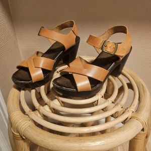 Ljusbruna sandaler med klack - Snygga beiga/bruna sandaler med klack och korsade remmar. De har en justerbar rem med spänne runt ankeln och en stabil klack för extra komfort. Material i kraftig läder. Perfekta till sommaren både till jeans och kjol/klänning.