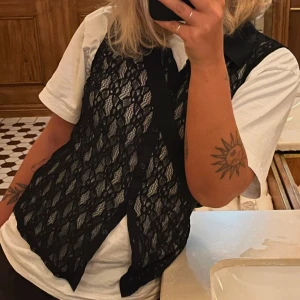 Svart spetsväst - Snygg svart spetsväst. Perfekt för att lägga till en elegant touch till din outfit. Västen har ett intrikat spetsmönster som ger en feminin och stilren look.