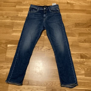 Mörk Blå jeans från Replay Thad  - Snygga blå jeans från Replay med klassisk femficksdesign och knappgylf. Jeansen har en rak passform och är perfekta för en avslappnad stil. Märkeslappen i läder baktill ger en extra touch.
