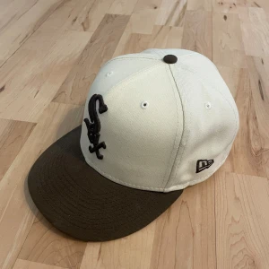 Vit och brun keps från New Era - Snygg vit keps från New Era med brun skärm och broderad logga på framsidan. Kepsen är en del av Cooperstown Collection och har en rosa insida på skärmen. Perfekt för att ge din stil en sportig touch. Skriv privat om du har frågor eller funderingar!