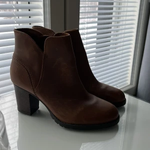 Bruna boots från Clarks - Snygga bruna boots från Clarks med dragkedja på sidan och en stabil klack. Perfekta för höst och vinter, dessa boots är både stiliga och bekväma.