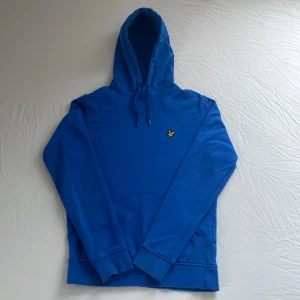 Blå hoodie från lyle&scott - Säljer en snygg blå hoodie. Tröjan har en klassisk känguruficka och en bekväm huva med dragsko. Perfekt för en avslappnad stil. Har en liten fläck som ni kan se på sista bilden men inget man märker av vid användning (: