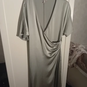 Grå/ljus grön omlottklänning - Elegant grå omlottklänning med korta ärmar och v-ringning. Klänningen har ett knytband i midjan, så man kan justera den. Har använts en gång. 