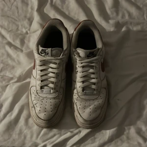 Nike Air Force 1 by you Röd swoosh - Röd swoosh och lädret runt Nike Air loggan bak. Storlek 43. Använda en del och lite slitna, men en enkel tvätt kan nog ändra detta.