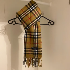 Burberry - Säljer en klassisk beige halsduk från Burberry . Den är gjord av 100% kashmir. Den har fransar i ändarna och är perfekt för att hålla dig varm och stilren under kyliga dagar. Hör av er vid minsta fundering☺️