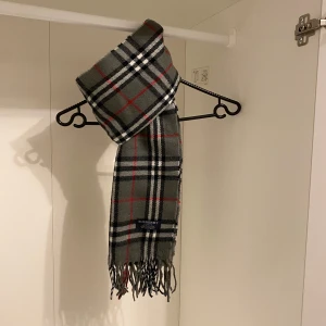 Burberry - Säljer nu denna Snygga halsduk från Burberry i färgen grå. Tillverkad i 100% mjuk kashmir med klassiskt fransad kant. Perfekt för att hålla dig varm och stilren under kyliga dagar. Hör av er vid funderingar☺️