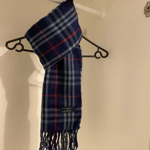 Burberry - Säljer nu denna Snygga halsduk från Burberry i blått. Tillverkad i 100% mjuk kashmir med klassiskt fransad kant. Perfekt för att hålla dig varm och stilren under kyliga dagar. Hör av er vid funderingar☺️