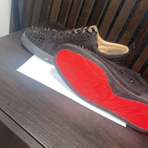 Svarta sneakers med nitar - Snygga svarta sneakers med nitar på ovansidan och en röd sula. Skorna har snörning och är tillverkade i skinn. Perfekta för att ge en edgy touch till din stil.