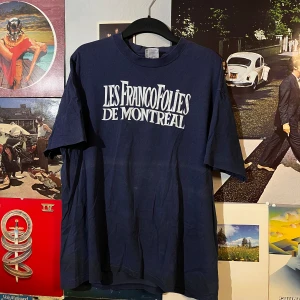 Blå t-shirt med tryck från Hanes - Säljer en blå t-shirt från Hanes med trycket 'Les FrancoFolies de Montreal' i vitt. T-shirten har en klassisk passform och korta ärmar, perfekt för en avslappnad stil.