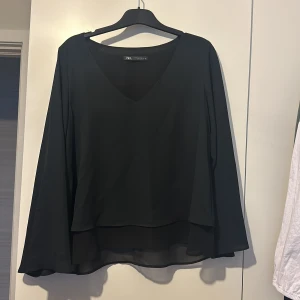 Svart blus från Zara - Elegant svart blus från Zara med v-ringning och långa vida ärmar. Perfekt för en stilren look. Tillverkad i ett lätt och luftigt material som ger ett fint fall🤩