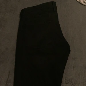 Svarta jeansbyxor - Snygga svarta jeansbyxor med klassisk femficksdesign och nitar vid fickorna. Perfekta för en stilren look. Midjan är normalhög och byxorna har en rak passform.