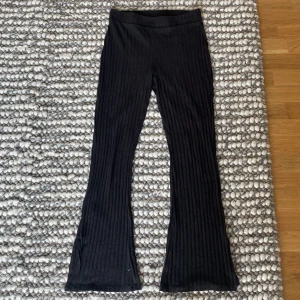 Svarta ribbade byxor från Gina Tricot - Säljer ett par svarta ribbade byxor från Gina Tricot i storlek M. De är superbekväma och har en hög midja som ger en snygg passform. Perfekta för både vardag och mysiga hemmakvällar. 🖤