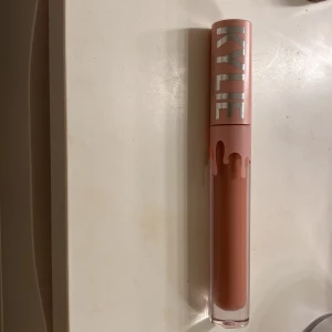 Läppglans från Kylie Cosmetics - Säljer ett snyggt läppglans från Kylie Cosmetics. Det har en härlig nude färg som passar perfekt till vardags eller fest. Förpackningen är stilren med ett rosa lock och Kylies logga i silver. Läppglanset ger en fin glans och känns mjukt på läpparna. Perfekt för att komplettera din sminksamling!❤️ den är knappt använd!!💕