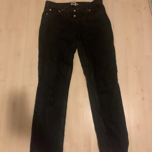 Svarta jeans från 157 - Säljer ett par svarta jeans från märket 157. De har en klassisk design med knappar framtill och en rak passform. Perfekta för både vardag och fest!