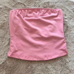 Rosa tubtopp - Säljer en söt rosa tubtopp. Perfekt för sommaren eller en festlig kväll. Den är gjord av mjukt och bekvämt material, vilket gör den idealisk för varma dagar. Toppen är axelbandslös och har en tight passform.