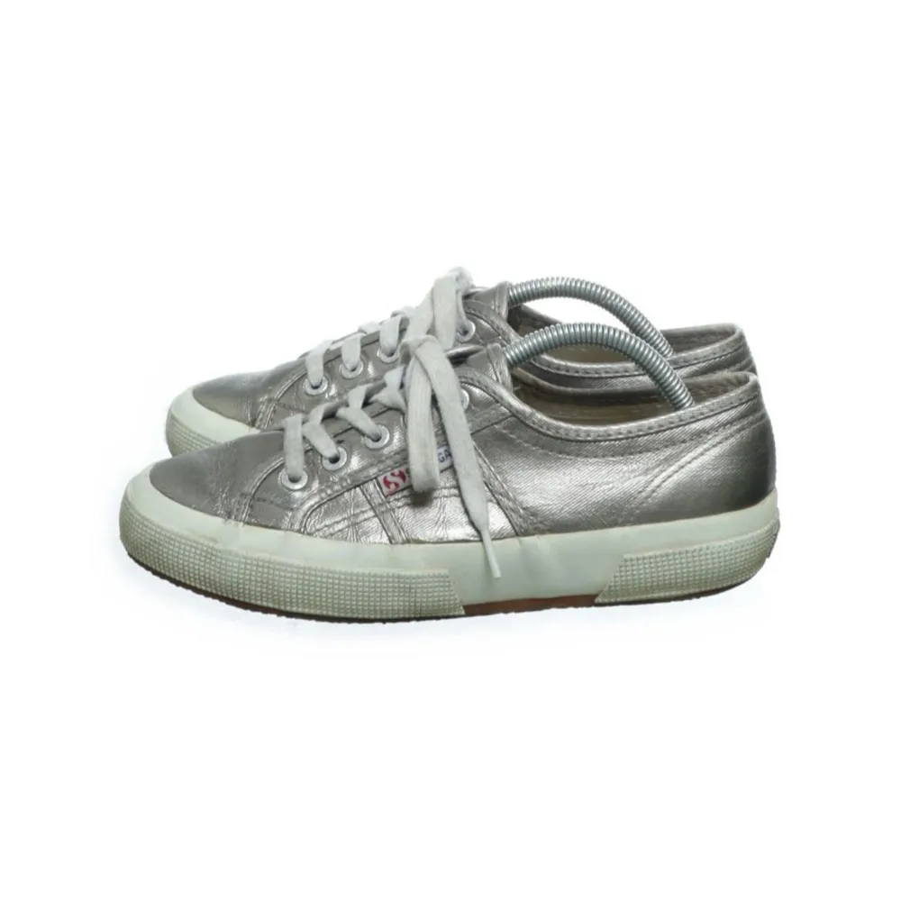 Säljer ett par snygga silvriga sneakers från Superga. De har en cool metallic-look och är gjorda av syntetmaterial. Skorna har snörning framtill och en bekväm vit sula. Perfekta för både vardag och fest!. Skor.