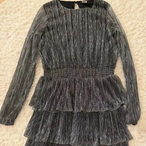Glittrig klänning från Lindex - Säljer en glittrig klänning från Lindex i en snygg silverfärg. Klänningen har långa ärmar och flera lager med volanger som ger en festlig look.Jag har använt den förra året på nyår sedan så hade jag växt ur den 🩷