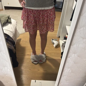 Blommig rosa kjol - Söt blommig rosa kjol med volangdetaljer. Perfekt för en somrig look. Kjolen har en luftig passform 