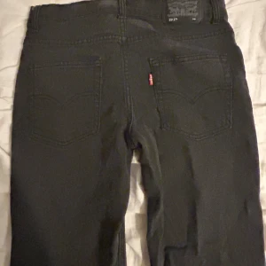 Svarta Levi's 551Z jeans - Snygga svarta Levi's 551Z jeans med en rak passform. Klassisk design med fem fickor och den ikoniska röda Levi's-loggan på bakfickan. Perfekta för en stilren look. Storlek är 14a