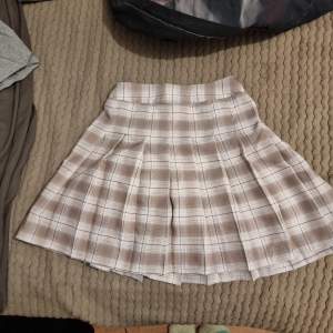 Säljer en söt beige rutig kjol med veckad design. Perfekt för en stilren och klassisk look. Kjolen har en kort längd och passar bra till olika tillfällen. Storleken är uppskattad, den är 140 i barnstorlek men passar xxs och xs
