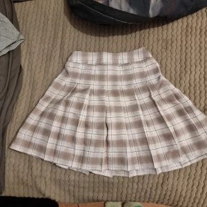 Beige rutig kjol - Säljer en söt beige rutig kjol med veckad design. Perfekt för en stilren och klassisk look. Kjolen har en kort längd och passar bra till olika tillfällen. Storleken är uppskattad, den är 140 i barnstorlek men passar xxs och xs