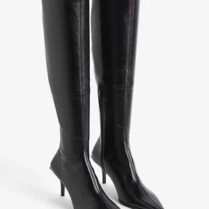 Boots H&M studio collection  - Snygga svarta knähöga sockboots från H&M studio collection  Stövlarna är i stretchigt läder och med en lätt lyster samt synliga sömmar, de har en smal klack på 8cm.  Spetsig tå med dragkedja vid sidan.  Endast använda en gång så i fint skick. Finns dock skav på ena klacken, se bild.  Köptes för 3000kr.