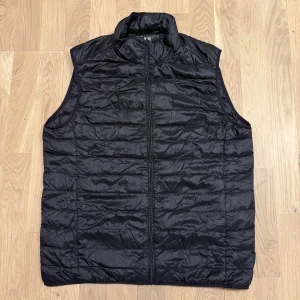 Svart dunväst från Uniqlo - Säljer en svart dunväst från Uniqlo. Västen är quiltad och har en dragkedja framtill. Perfekt för lager-på-lager under kyliga dagar. Den är lätt och smidig att bära med sig. Pris kan diskuteras.