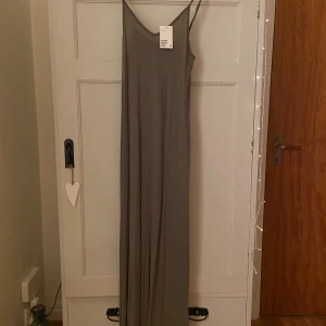 Khakigrön långklänning från H&M - Säljer en enkel khakigrön långklänning från H&M. Klänningen har smala axelband som går att reglera och en enkel design som passar perfekt för olika tillfällen. Materialet är mjukt och följsamt, 100% viskos, vilket ger en bekväm passform. Slits i båda sidorna.