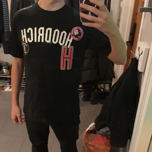 Svart Hoodrich t-shirt  - Snygg svart t-shirt med tryck och detaljer i vitt och rött. Perfekt för en avslappnad stil. 