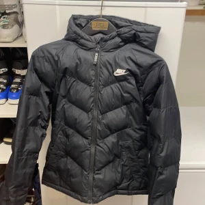 Svart dunjacka från Nike - Säljer en svart dunjacka från Nike med huva och dragkedja. Bra skick och i storlek 158-170 (XL i barnstorlek) hör av dig vid frågor 
