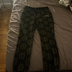 Svarta mönstrade byxor från Les Deux - Snygga svarta byxor från Les Deux med ett unikt mönster i grått. Byxorna har en bekväm passform med snörning i midjan och är perfekta för en stilren look. Märkesloggan är diskret placerad på sidan.