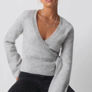 Grå omlottstickad tröja - Säljer en stilren grå omlottstickad tröja med lång ärm. Perfekt för kyligare dagar och ger en elegant look. Tröjan har en v-ringad design som passar bra till allt