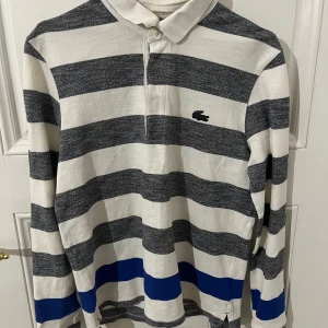 Pikétröja från Lacoste - Säljer en stilig pikétröja från Lacoste. Tröjan är lång ärmad och har en klassisk krage med knappar. Perfekt inför våren och sommaren. Storlek S men ganska stor i storleken, passar perfekt på den som är mellan 170-180cm. Bara att höra av dig vid fundering