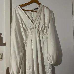 Vit omlottklänning från Gina Tricot - Elegant vit omlottklänning från Gina Tricot med långa ärmar och v-ringad design. Perfekt för en stilren look med sitt mjuka och glansiga material. Perfekt till t.ex. studenten!💕 Väldigt bra skick