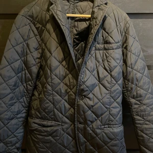 Svart quiltad jacka från Polo Ralph Lauren - Säljer en stilren svart quiltad jacka från Polo Ralph Lauren. Jackan har en klassisk design med knappar framtill och två fickor. Perfekt för kyligare dagar.