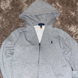 Grå hoodie från Ralph Lauren - Säljer en grå zip hoodie från Ralph lauren. Storlek 14-16 år (xs) men är lite liten i storleken. Den är i bra skick har inte använt den jättemycket men den är inte trasig på nått sätt och har heller inga fläckar. Skicka meddelande om ni har några frågor eller vill ha fler bilder.