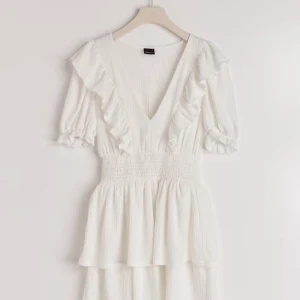 Vit klänning från Gina Tricot - Säljer en söt vit klänning från Gina Tricot med volanger och v-ringning. Den har varit använd max 3 gånger på grund av att jag har andra klänningar. Klänningen har korta ärmar och en smockad midja som ger en fin passform. Perfekt för sommaren eller fest!❤️ Köptes helt ny i butik för 399. 