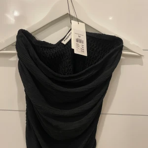 Svart topp från Kappahl - Snygg svart top från Kappahl med en unik textur. Perfekt för en stilren look. Toppen  har en elegant drapering och är tillverkad i ett bekvämt material.