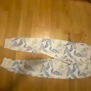 Mönstrade mjukisbyxor med löv - Säljer ett par bekväma mjukisbyxor med ett färgglatt lövmönster i blått, grönt och grått. Perfekta för en avslappnad dag hemma. Byxorna har en elastisk midja för extra komfort.