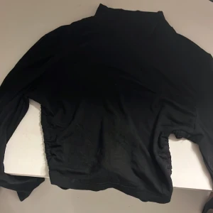 Svart långärmad topp med snörning - Snygg svart långärmad topp med snörning i sidorna. Perfekt för en stilren look. Toppen har en hög krage. Nästan aldrig använd eftersom den är mer festlig. Fråga om bilder💕